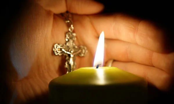 Hořící svíčka na pozadí s rukou kříž — Stock fotografie