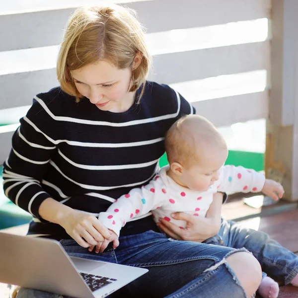 年轻的母亲与她的宝贝女儿工作或学习上的笔记本电脑 — 图库照片