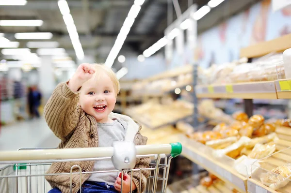 Niño sentado en el carrito de la compra en un supermercado —  Fotos de Stock