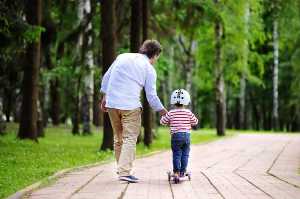 Padre mostrando a su hijo pequeño cómo montar un scooter — Foto de Stock