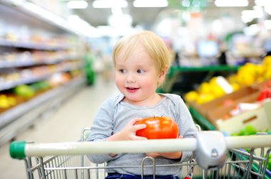 Bir süpermarkette alışveriş sepeti oturuyor ve yürümeye başlayan çocuk