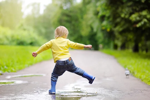 Kleiner Junge in Regenstiefeln springt in Wasserbecken — Stockfoto