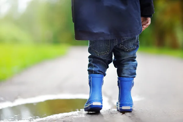 Niño con botas de lluvia de pie cerca de un charco — Foto de Stock