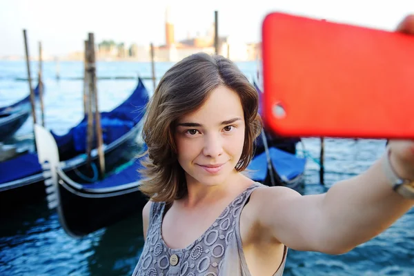 Ung kvinne som lager selfiefotografi med gondoler på bakgrunn av Venezia, Italia – stockfoto