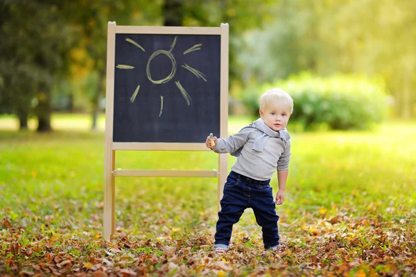 Toddler boy drawing standing by a blackboard — Stock Photo, Image