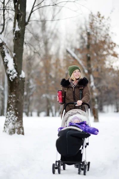 冬の公園でベビーカーで赤ちゃんと一緒に歩いて若い母親 — ストック写真