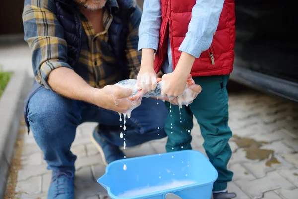 Preschooler boy helping his father washing family car. Little dad helper. Family with children spends time together in the backyard