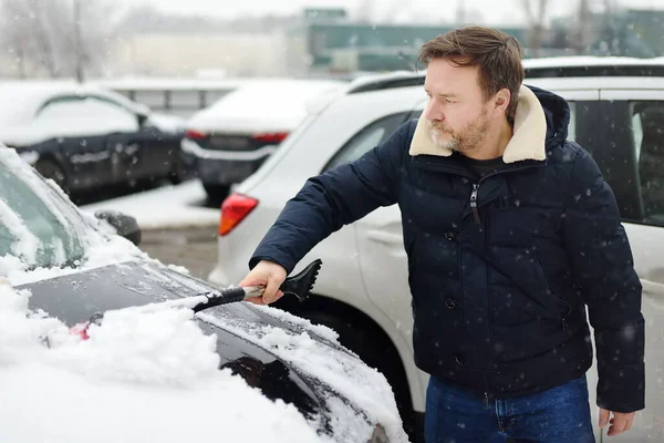 大人の男は雪の後にブラシで車をきれいにします 自動車のフードに吹雪の後に雪のドリフト 雪嵐の後 市内の道路上の困難な交通状況 — ストック写真