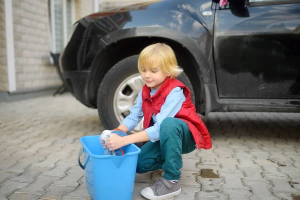 ガレージの近くで黒い車を洗っている小さな男の子 子供は楽しさと彼の両親を助ける 家族の育て方 仕事に子供を教える — ストック写真