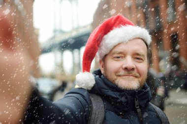 Noel Baba şapkalı bir adam kar yağarken New York 'ta Manhattan Köprüsü yakınlarında selfie çekiyor. New York 'ta kış Xmas tatili. New York 'ta yeni yıl tatili.