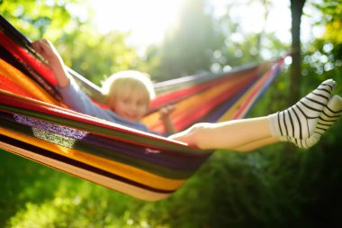 Sarışın, sevimli beyaz çocuk arka bahçede ya da dışarıda renkli hamakla eğleniyor. Çocuklar için açık havada aktif yaz tatili. Çocuk dinleniyor ve hamakta sallanıyor.