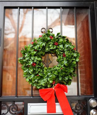 Ön kapısında kırmızı kurdele olan yeşil Noel çelengi. Kış tatili için dekore edilmiş evin girişi. Noel ve Yeni Yıl için Amerikan evinin tipik dekorasyonu..