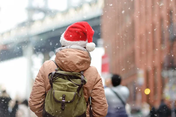 圣诞前夕 一名戴着圣诞老人帽子的年轻女性游客在纽约的一场降雪中散步 在下雪天 曼哈顿大桥和纽约的摩天大楼 纽约的寒假在纽约 雪很少见 — 图库照片