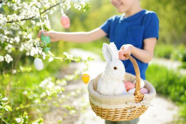 Paskalya bayramında bahar parkında paskalya yumurtası avlarken elinde beyaz oyuncak tavşanla sepet tutan sevimli çocuk. Geleneksel Paskalya festivali..