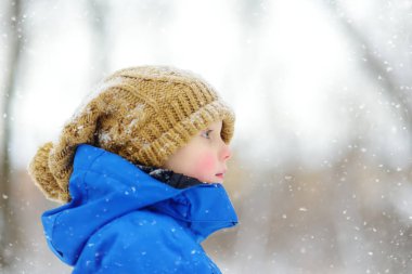 Funny little boy with frostbitten cheeks in blue winter clothes walks during a snowfall. Frost wintertime. Outdoors winter activities for kids. clipart