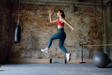 HIIT antrenmanı sırasında sportif bir kadındı. Dinamik hareket. Sporcu kadın spor salonunda yüksek atlama sürecinde