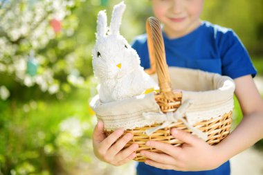 Paskalya günü bahar parkında renkli yumurta avında elinde beyaz oyuncak tavşanla sepet tutan sevimli küçük çocuk. Paskalya festivali boyunca çocuklar için geleneksel eğlence.