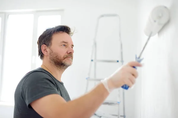 一个英俊而成熟的男人在公寓里修理房子的画像 那个人用胶辊把墙壁涂成白色 你自己来吧Diy 用他们的手修理 — 图库照片