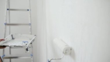 Evde tamirat yapan yakışıklı, olgun bir adam. Duvarı silindirle beyaza boyuyor. Kendiniz yapın. Diy. Elleriyle tamir ederler..