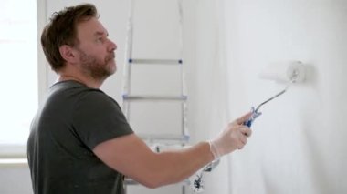 Evde tamirat yapan yakışıklı, olgun bir adamın portresi. Duvarı silindirle beyaza boyuyor. Kendiniz yapın. Diy. Elleriyle tamir ederler..