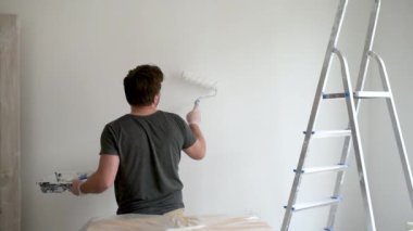 Evde tamirat yapan yakışıklı, olgun bir adamın portresi. Duvarı silindirle beyaza boyuyor. Kendiniz yapın. Diy. Elleriyle tamir ederler..