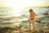 Az óvodás fiú felfújható gyűrűvel úszni megy a tengerbe. Szórakoztató tengerparti nyaralás gyerekeknek. Nyaralás gyermekes családoknak.