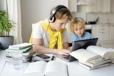 Ergen çocuk evde ders çalışıyor. Onun küçük erkek kardeşi yakında oynuyor. Evde eğitim. Çevrimiçi eğitim ve tecrit sırasında çocuklar için uzaktan öğrenme. Yaş farkı olan kardeşlerin dostluğu..