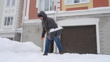 Güçlü bir kar fırtınası sırasında, evin yakınındaki yolu temizleyen olgun bir adam. Yoldan kar kürüyen bir adam. Büyük kar yığınları. Kar fırtınası sonrası şehirde zor bir durum