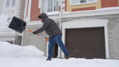 Güçlü bir kar fırtınası sırasında, evin yakınındaki yolu temizleyen olgun bir adam. Yoldan kar kürüyen bir adam. Büyük kar yığınları. Kar fırtınası sonrası şehirde zor bir durum