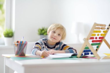 İlkokul öğrencisi evde ödev yapıyor. Çocuk saymayı öğreniyor, aritmetik örnekler çözüyor, çalışma kitabı alıştırmaları yapıyor. Matematik dersi. Anaokulu bebeğini okula hazırlamak. Çocuklar için eğitim.