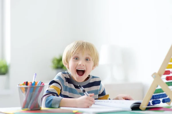 Excited elementary school boy doing homework at home. The child is passionate about the learning process. Delighted with what he does. Preparing a preschooler for school. Education for kids