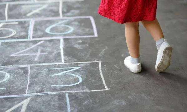 Closeup of little girl\'s legs and hop scotch drawn on asphalt. Child playing hopscotch game on playground outdoors on a sunny day. Summer activities for children.