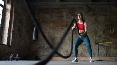 Spor salonunda savaş halatlarıyla egzersiz yapan genç bir kadın. Güçlü bayan sporcu savaş halatıyla çapraz formda idman yapıyor. Normal spor bağışıklık sistemini güçlendirir ve hastalıklara karşı iyi sağlık ve direnç sağlar. Sağlıklı yaşam tarzı