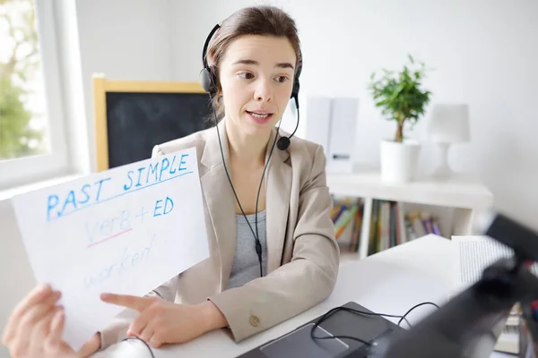 Young woman is teaching english with laptop computer, camcorder and headphone at home. Teacher is having video conference chat with student. Homeschooling. Online education.