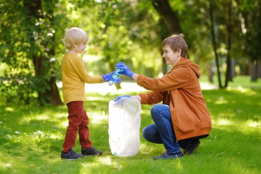 Gönüllü bir kadın ve küçük bir çocuk plastik çöpü alıp dışarıdaki çözünebilir çöp torbasına koyuyorlar. Ekoloji, geri dönüşüm ve doğa kavramının korunması. Çevre koruma.
