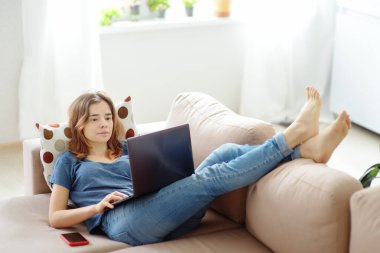 Dizüstü bilgisayarla çalışan bir kadın evdeki kanepede yatıyor. Serbest çalışan ya da blogcu. Mesafe öğrenme. Ek eğitim. Geri çekiliyoruz. Yetişkinler için internet işi. Sosyal medya bağımlılığı