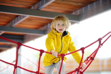 Sevimli anaokulu çocuğu dışarıda oyun parkında eğleniyor. Çocuklar için bahar / yaz / sonbahar aktif spor eğlencesi. Çocuklu aile aktivitesi. Çocuklar için eğlence parkı ekipmanı.