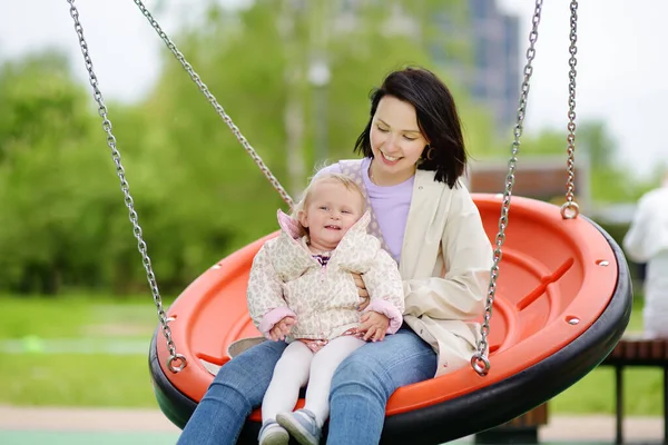 屋外の遊び場で楽しんでいる幼児の女の子 若い母親はスイングに娘に乗る 秋小さな子供を持つ家族のためのアクティブなレジャー 幸せな母親 — ストック写真