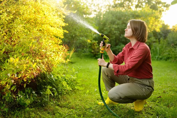 Wanita Muda Tukang Kebun Menyiram Tanaman Dengan Selang Dengan Sprinkler — Stok Foto