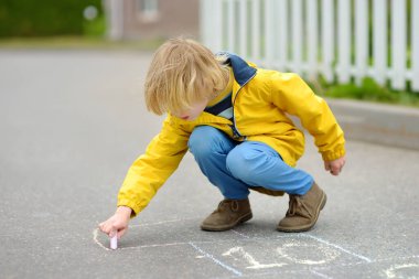 Küçük çocuk asfalta renkli tebeşirle seksek oynuyor. Çocuk bir bahar günü dışarıda oyun bahçesinde seksek oynuyor. Çocuklar için açık hava aktiviteleri.