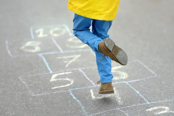 Little boy\'s legs and hopscotch drawn on asphalt. Child playing hopscotch game on playground on spring day. Outdoors activities for children.