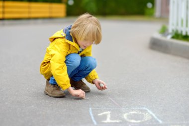Küçük çocuk asfalta renkli tebeşirle seksek oynuyor. Çocuk bir bahar günü dışarıda oyun bahçesinde seksek oynuyor. Çocuklar için açık hava aktiviteleri.