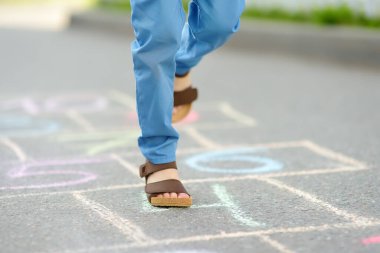 Küçük çocuğun bacakları ve asfalta çizilmiş seksek viskisi. Çocuk bahar günü oyun bahçesinde seksek oynuyor. Çocuklar için açık hava aktiviteleri.