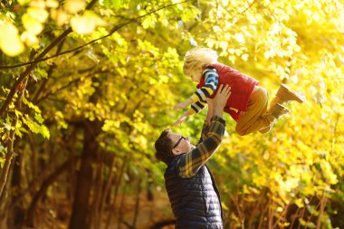 Little boy and his father having fun during stroll in the forest on sunny autumn day. Dad throws child up. Quality family time outdoor. Hiking with kids.