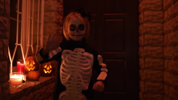 Little child in scary skeleton costume at Halloween celebration party. The child is ready for trick or treat on Halloween night. The kid waves his hand before knocking on the door of the house — Stock Footage Little Child Scary Skeleton Costume Halloween Celebration Party Child Ready Royalty Free Stock Footage