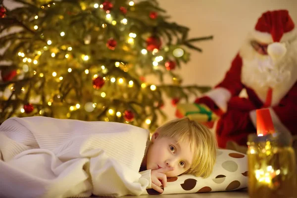 圣诞前夕 小男孩在树下等圣诞老人 圣诞老人带来了礼物 孩子不睡觉 但他没有表现出来 圣诞节或新年之夜的魔法 寒假的传统 — 图库照片