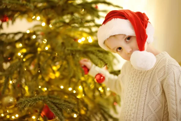 小男孩戴着圣诞礼帽 准备庆祝圣诞节 可爱的孩子用玻璃玩具装饰圣诞树 在新年的夜晚 婴儿对魔法和礼物的希望 寒假前后的传统 — 图库照片