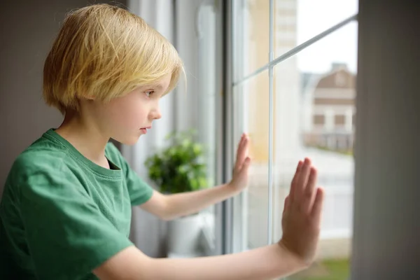 悲しい小さな男の子が窓の近くに座って通りを見ていた 家で寂しい 友達も兄弟もいない 家族の中の1人の赤ん坊 子供は仲間との関係を築くことができない 動揺したガキだ うつ病 — ストック写真