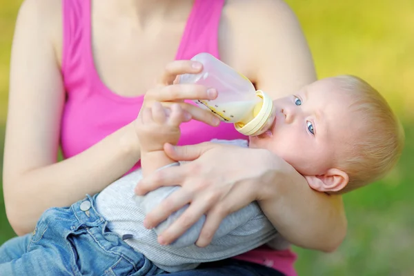 Baby drinking milk from bottle in mother hands — Stock Photo, Image