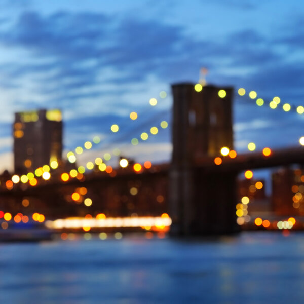 Bokeh photo of New York City Brooklyn Bridge with downtown skyline over East River at night